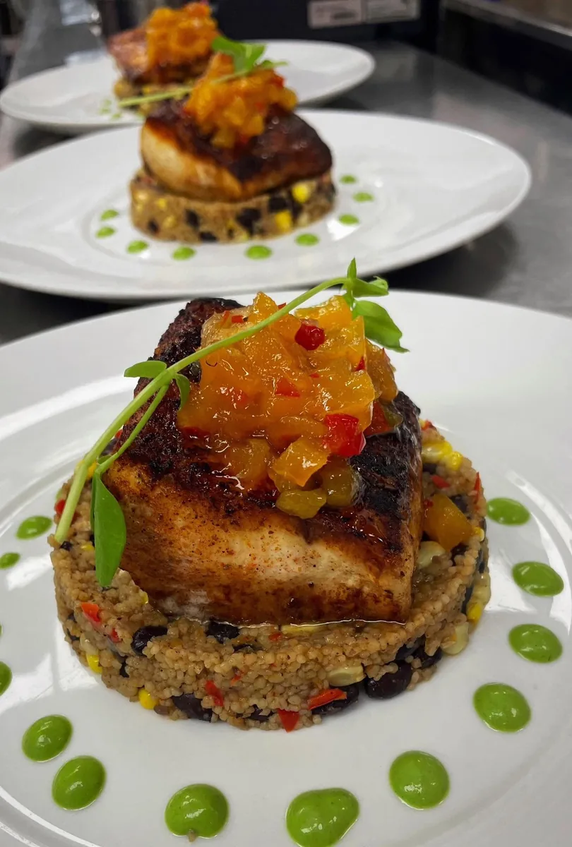 A blackened mahi-mahi fillet topped with a mango and pepper relish on a round of couscous with black beans and corn