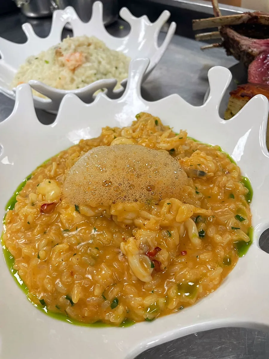A seafood risotto topped with a light foam in a white splash-shaped bowl