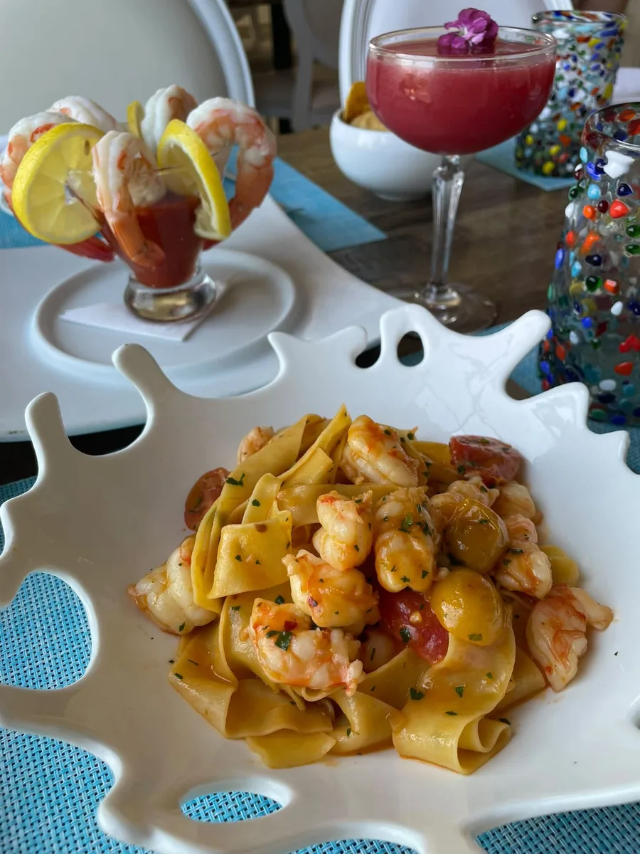 Gulf shrimp with cherry tomatoes over pappardelle, with a shrimp cocktail and a red cocktail behind