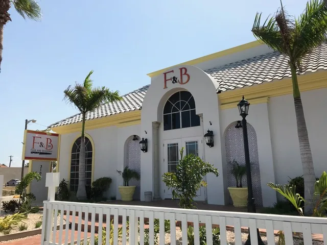 The white F&B building with arched windows, palm trees and a white picket fence on Padre Boulevard
