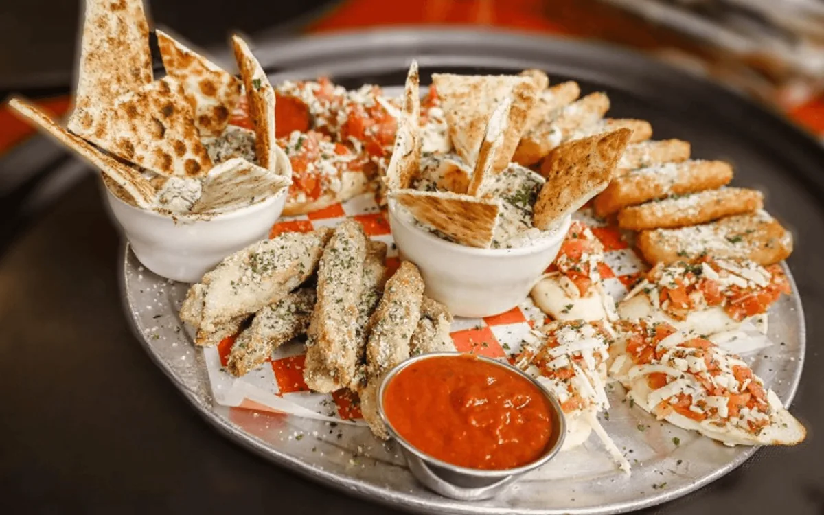 An appetizer platter with bruschetta, breaded fried mozzarella and other fried strips, flatbread with two dips and a cup of marinara