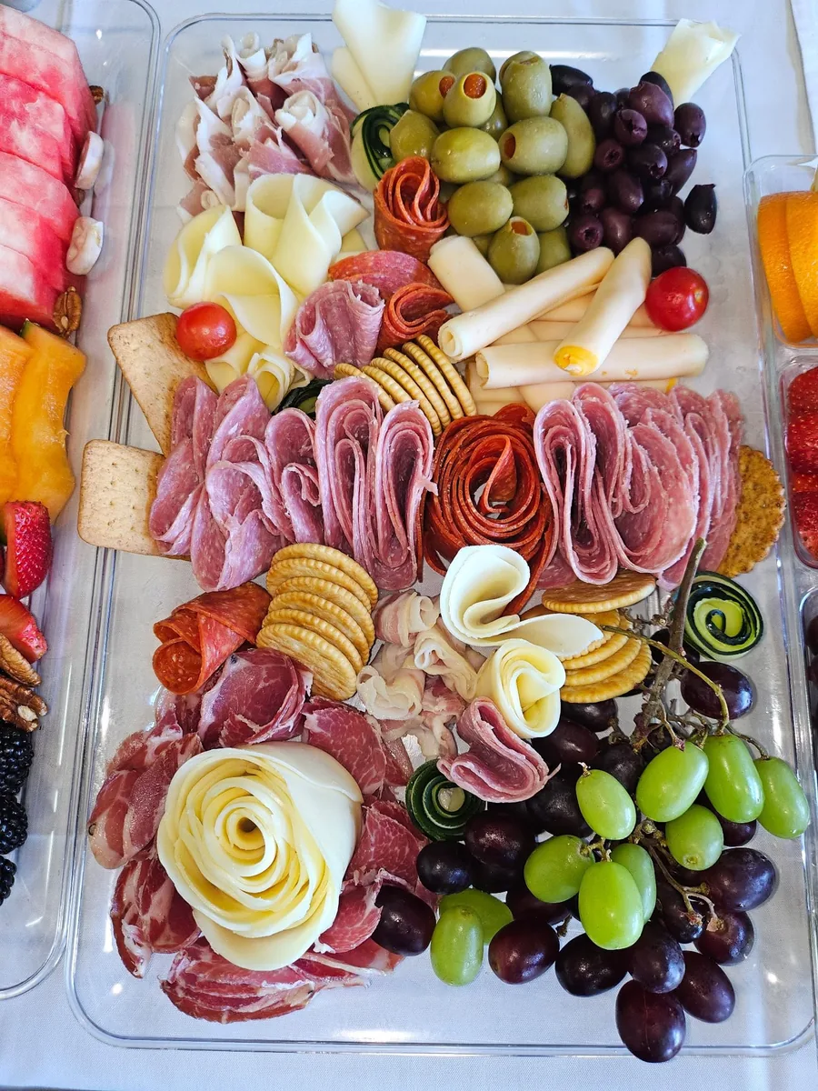 A charcuterie platter of folded salami and capicola, cheese roses, olives, crackers and grapes