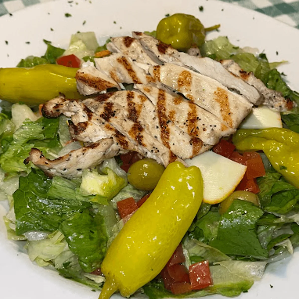 Sliced grilled chicken over a green salad with pepperoncini, green olives and diced tomatoes