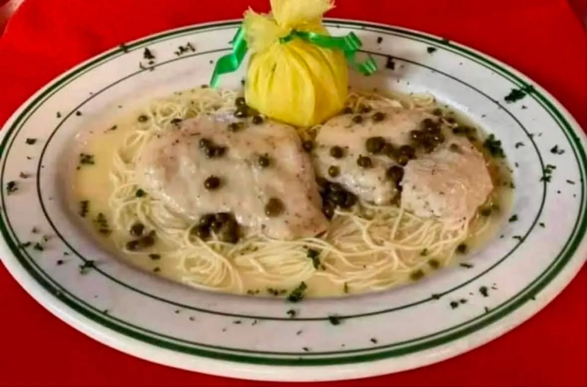 Two cutlets in a lemon-butter caper sauce over angel hair pasta, with a lemon half wrapped in cheesecloth