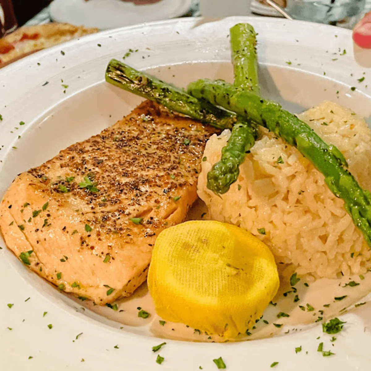 A seared salmon fillet with grilled asparagus, rice and a lemon half wrapped in cheesecloth