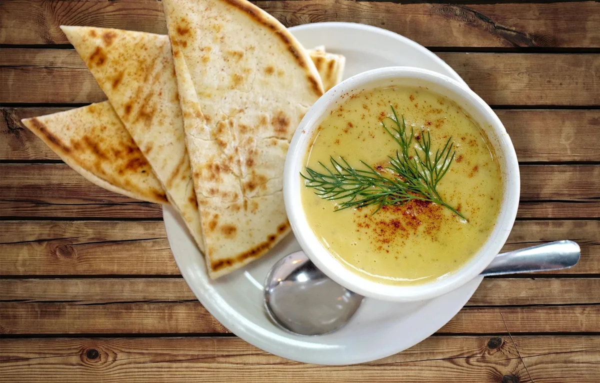 A cup of butternut squash soup with a dill sprig, served with toasted pita wedges