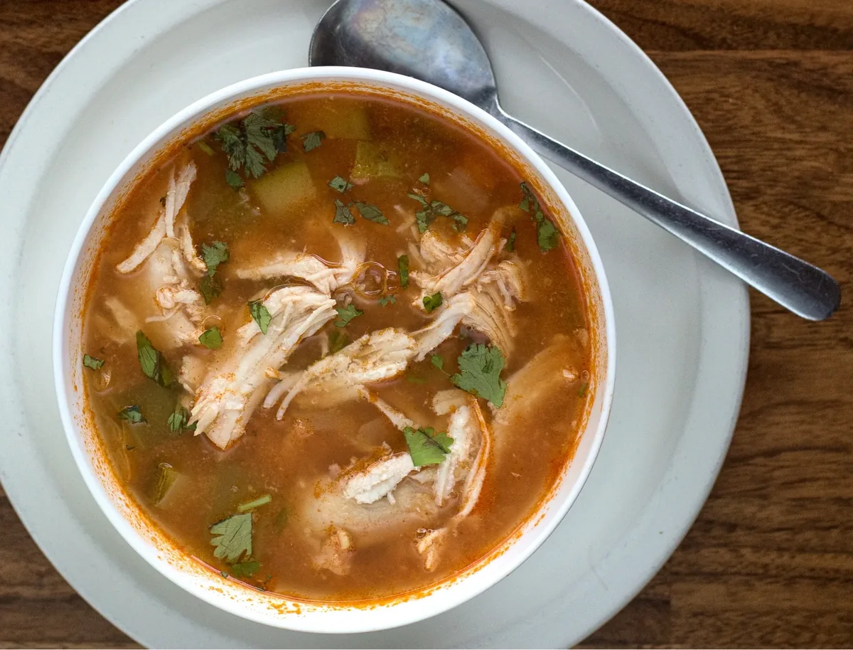 A bowl of chicken soup with shredded chicken and cilantro in a red broth