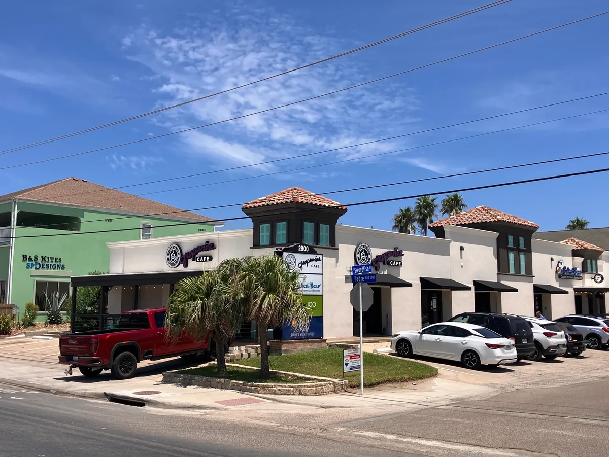 The Grapevine Cafe storefront on a sunny day, a white building with tile-roof towers and palm trees