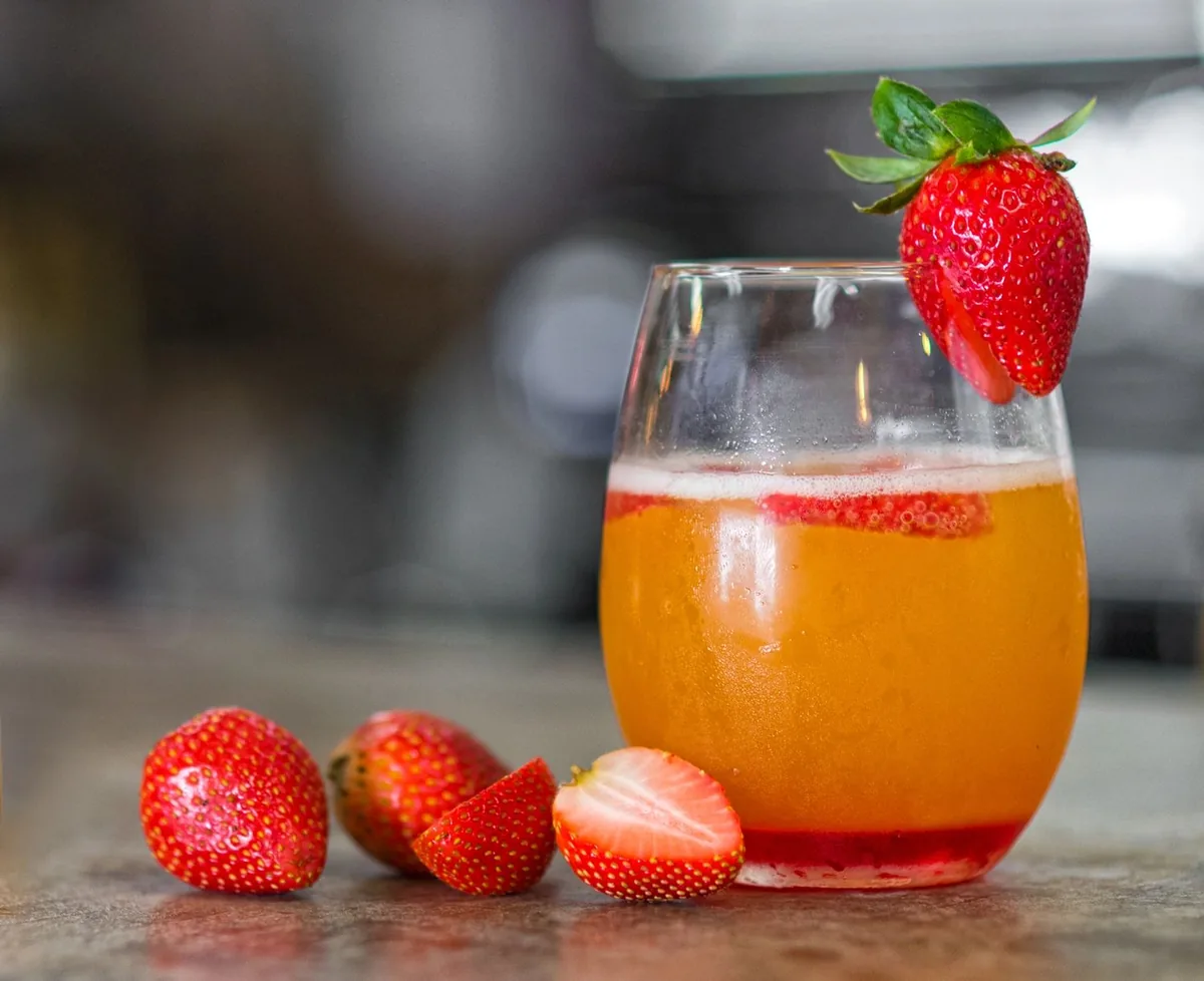 An orange drink with fresh strawberries in a stemless glass