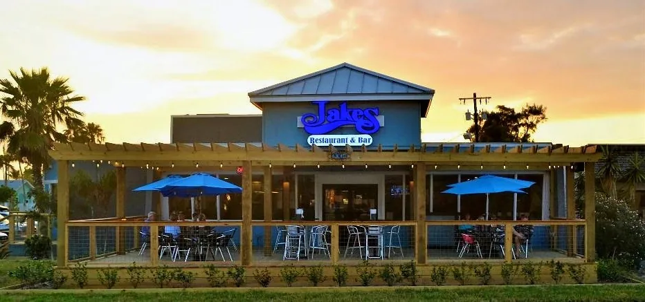 The front of Jake's Restaurant & Bar at sunset, with its covered patio, blue umbrellas and blue Jakes sign