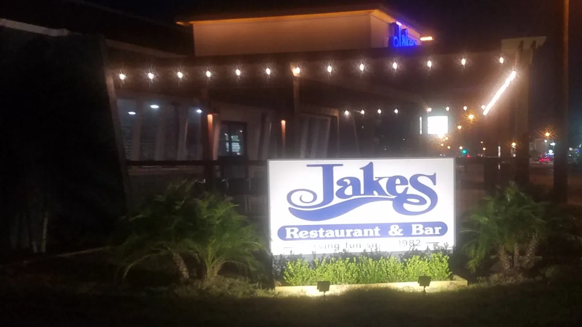 The lit Jakes Restaurant & Bar sign at night, with string lights over the patio behind it