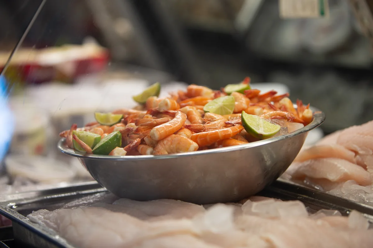 A steel bowl of boiled shrimp with lime wedges in the seafood case