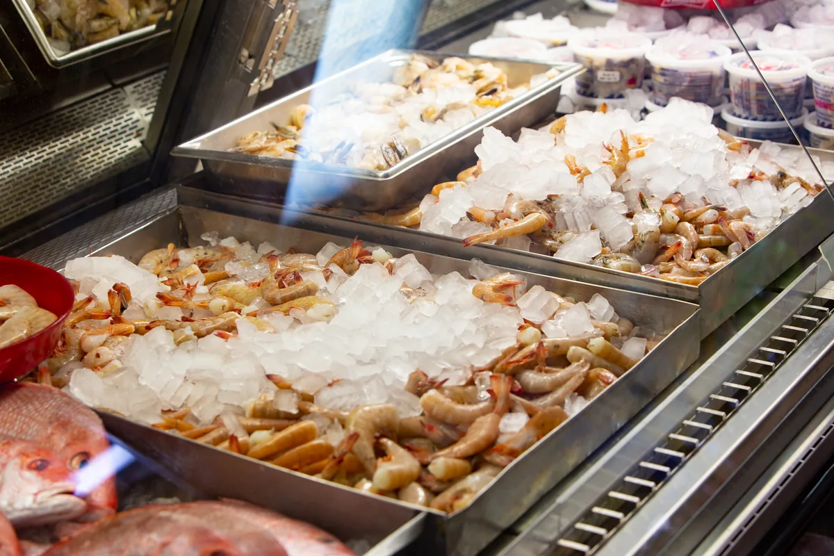 Trays of fresh shrimp on ice in the market's display case, with a red snapper in front