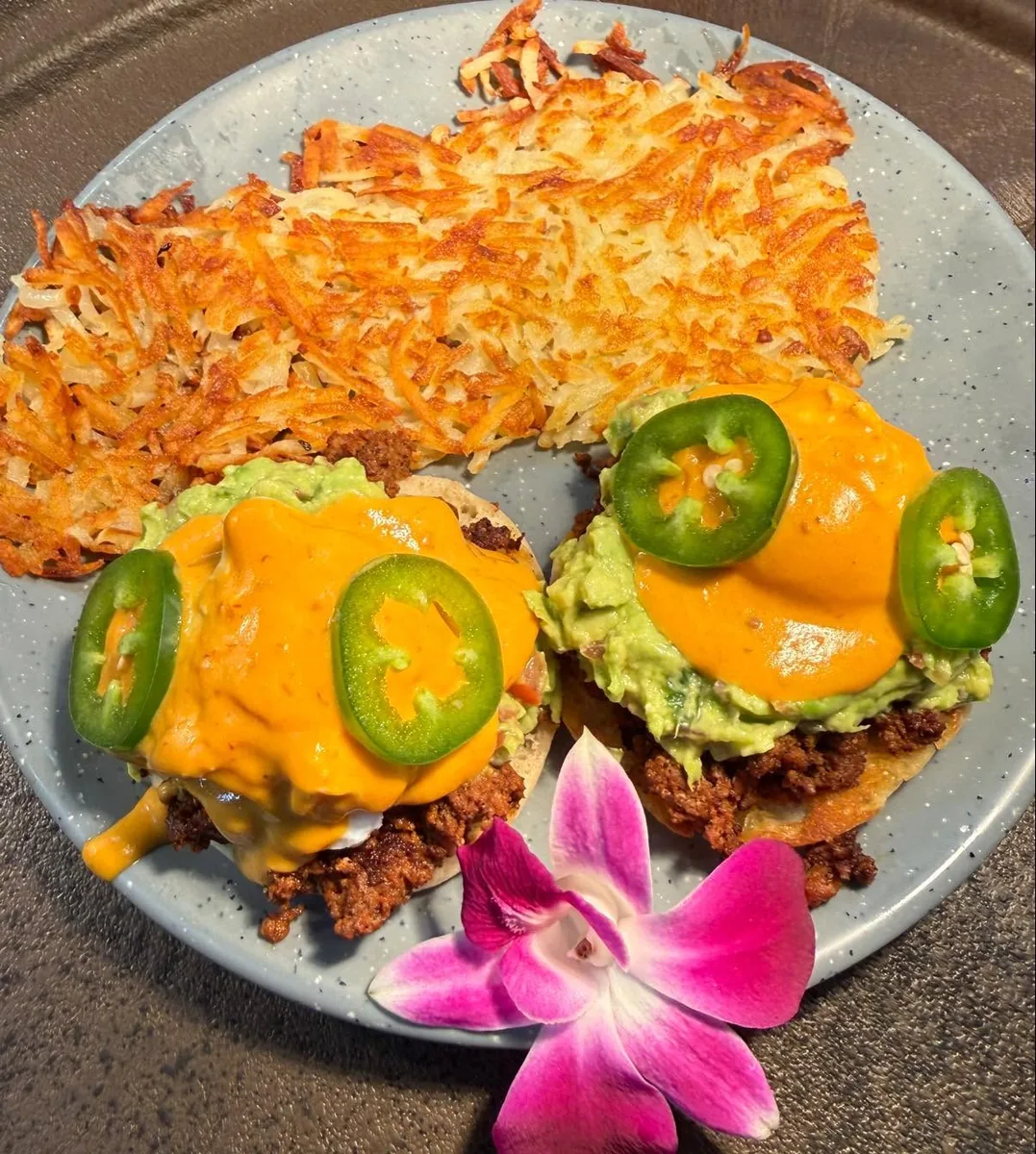 Two English-muffin benedicts with seasoned meat, guacamole, orange hollandaise and jalapeño slices, with hash browns