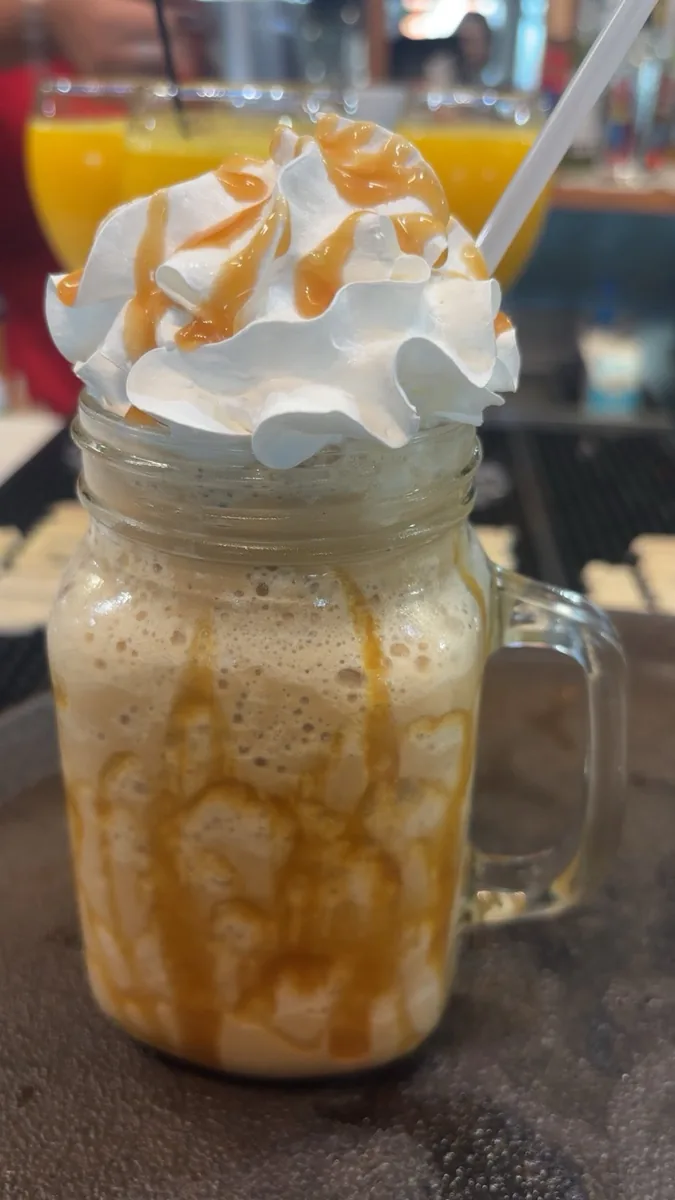 A caramel frappe in a mason jar mug, topped with whipped cream and caramel drizzle