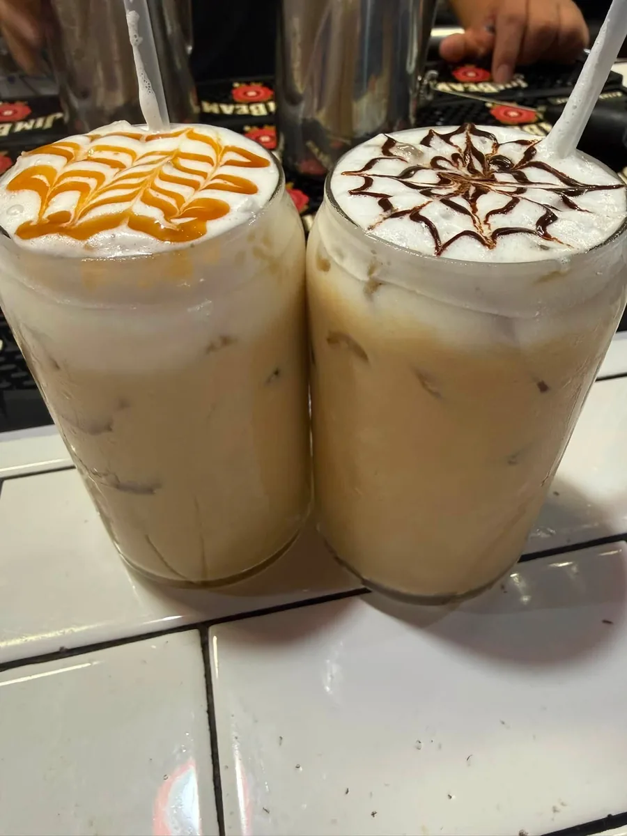 Two iced lattes with caramel and chocolate drizzle designs on the foam