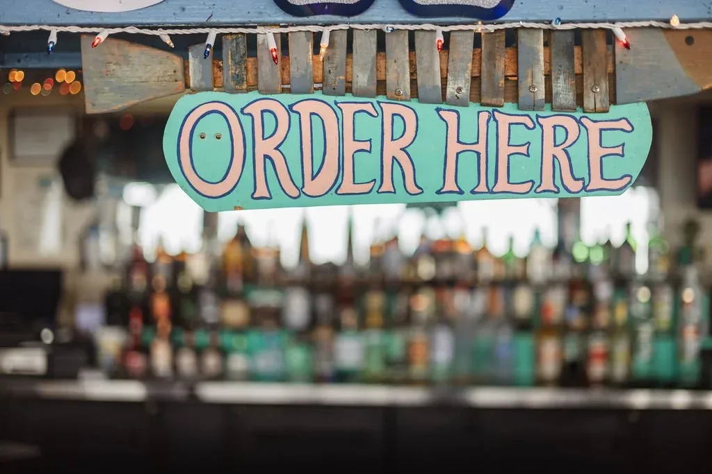 A hand-painted Order Here sign hanging over the bar, with bottles behind it