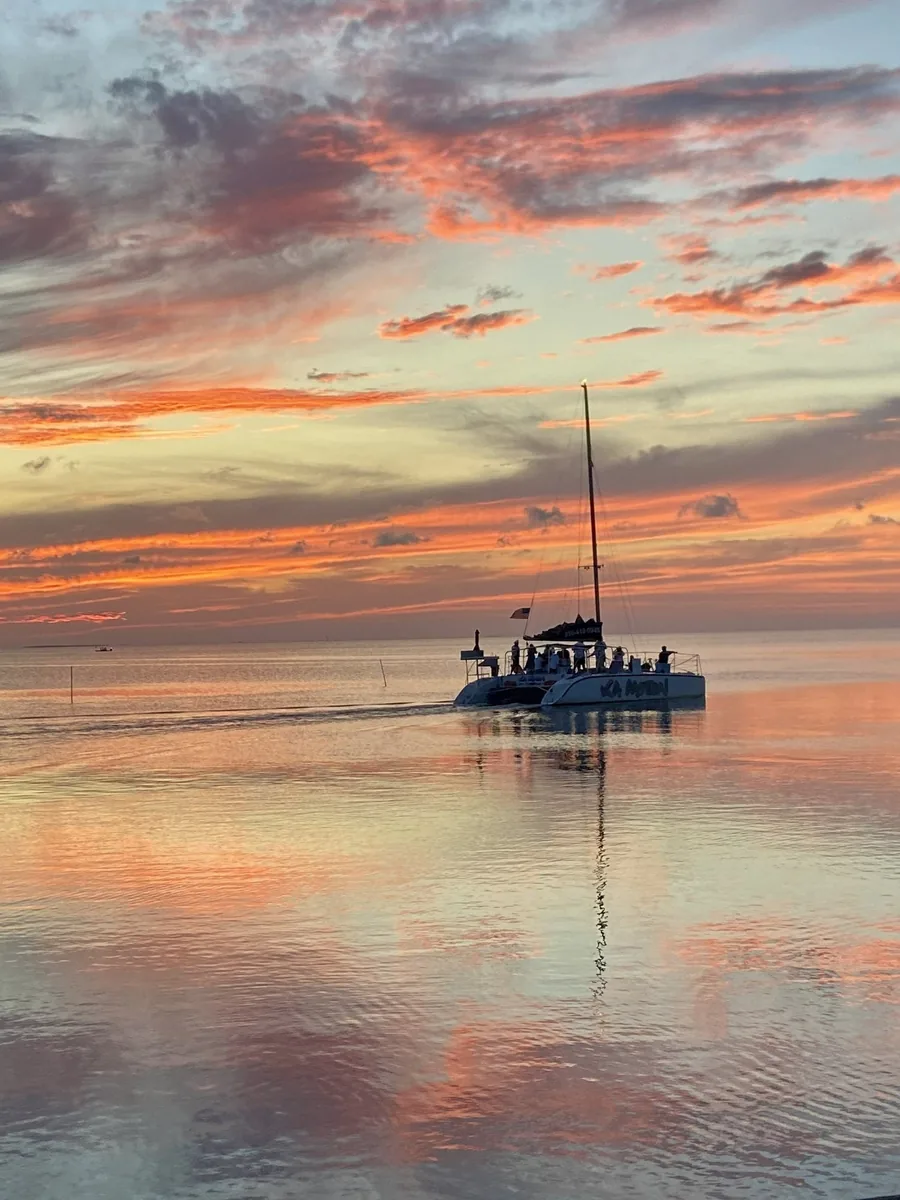 A sailing catamaran on still water under a pink and orange sunset sky