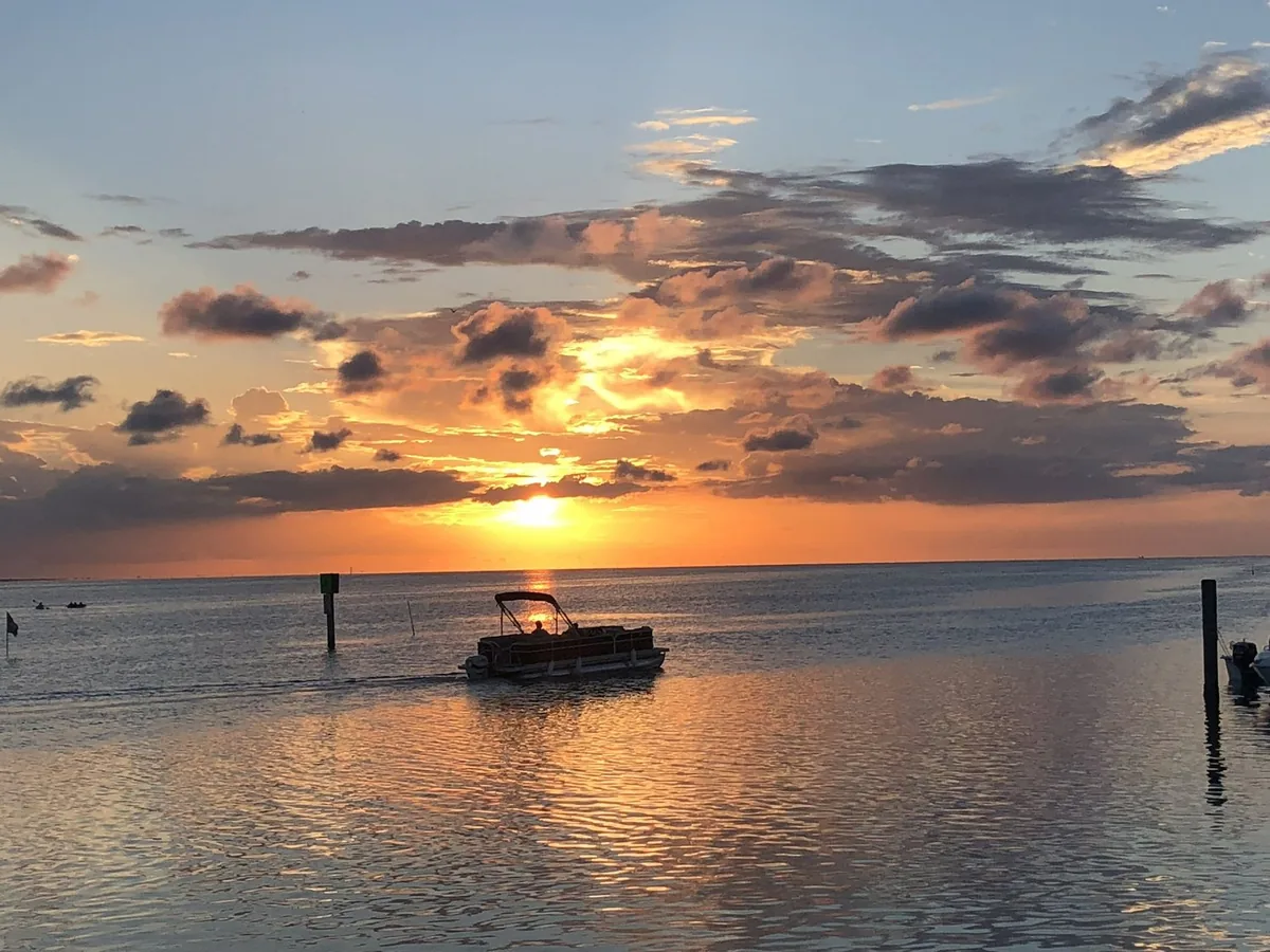 A pontoon boat heading out under a golden sunset over the bay