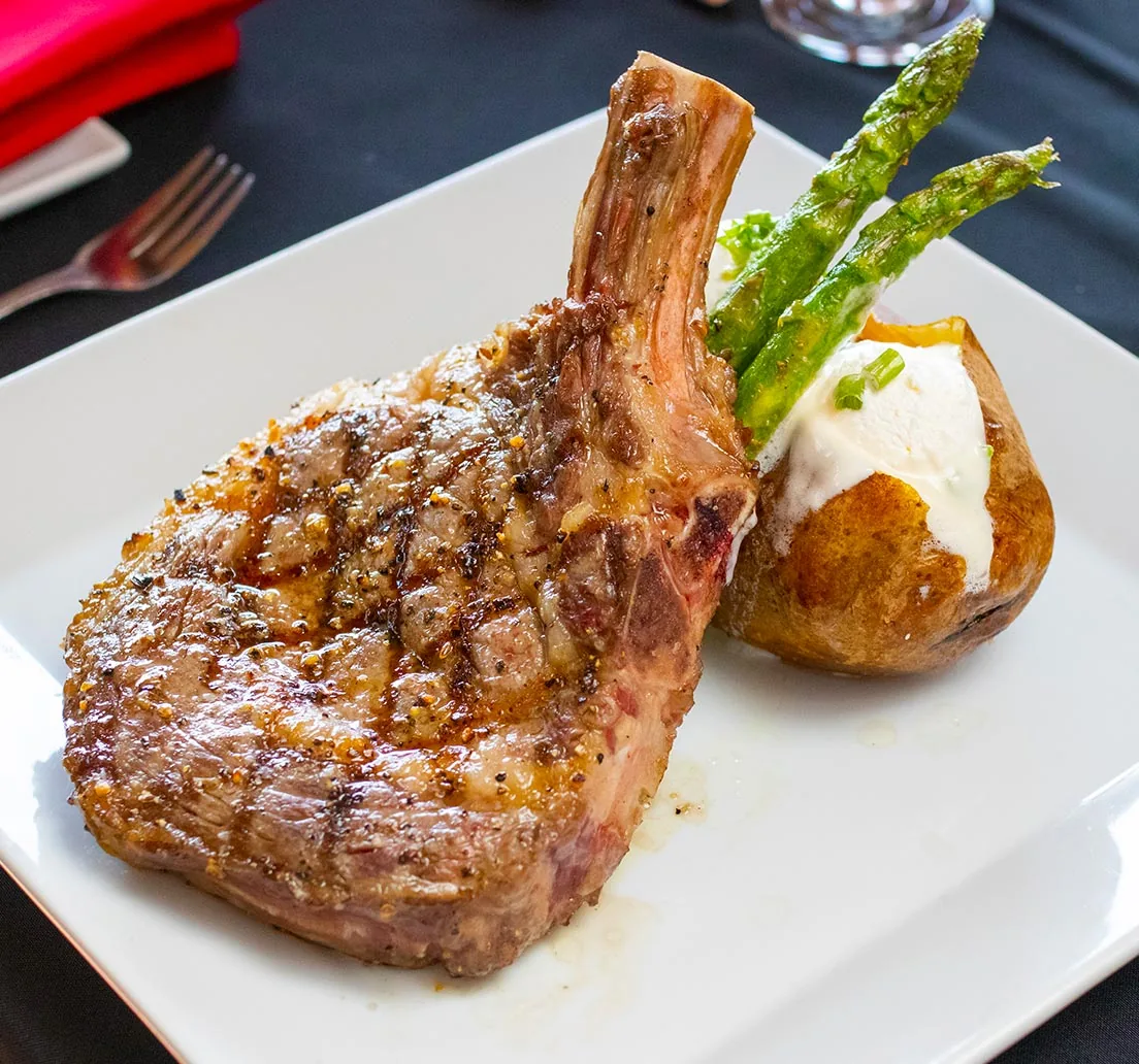 A grilled bone-in steak with a baked potato topped with sour cream and chives, and asparagus