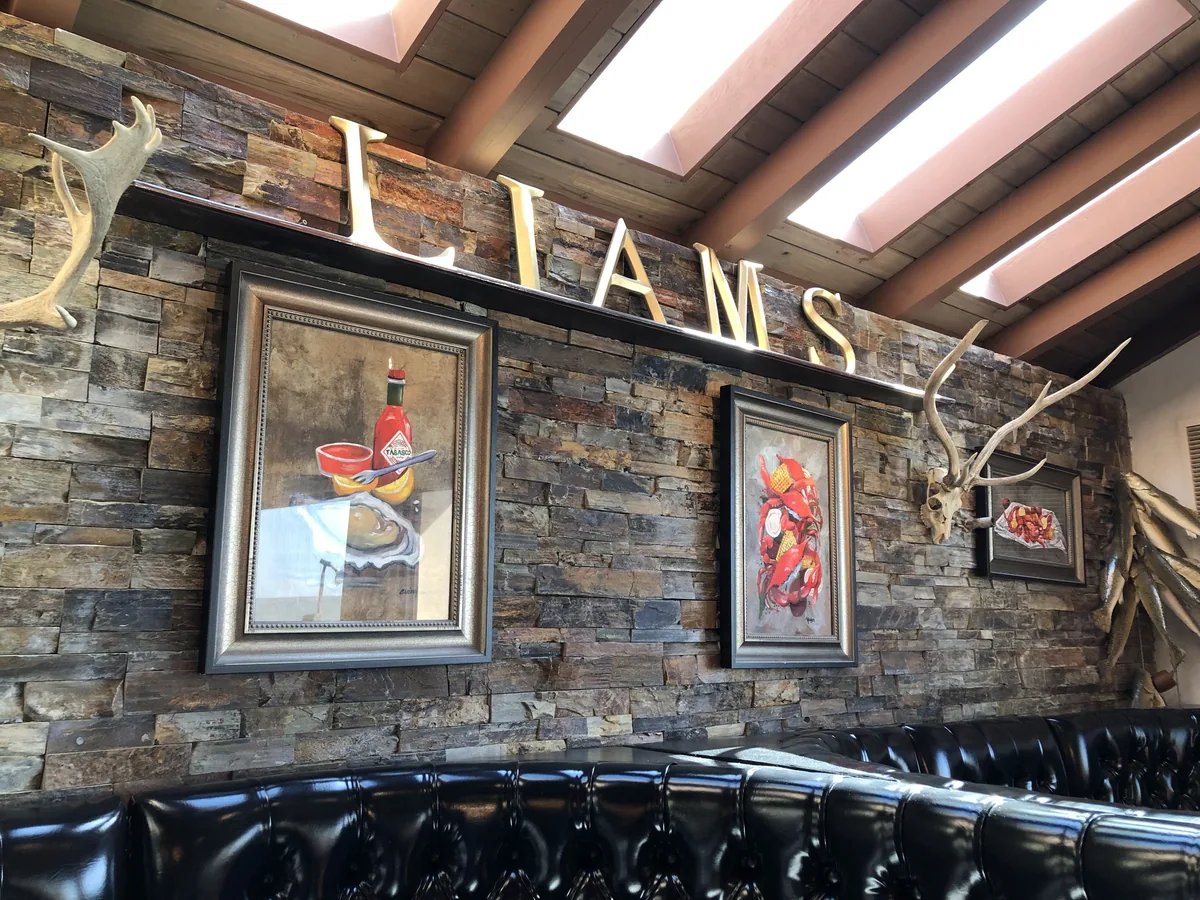 The dining room wall with gold LIAMS letters, stacked stone, framed seafood paintings, antlers and black tufted booths