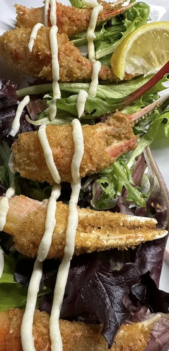 Breaded fried crab claws drizzled with a white sauce on spring mix, with a lemon wedge