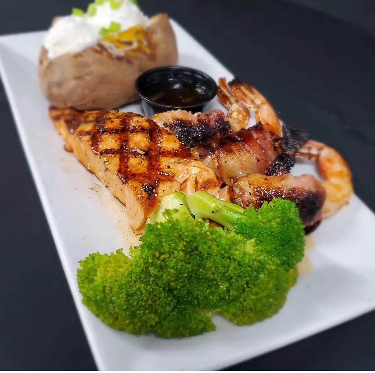 A grilled salmon fillet with bacon-wrapped shrimp, broccoli and a baked potato