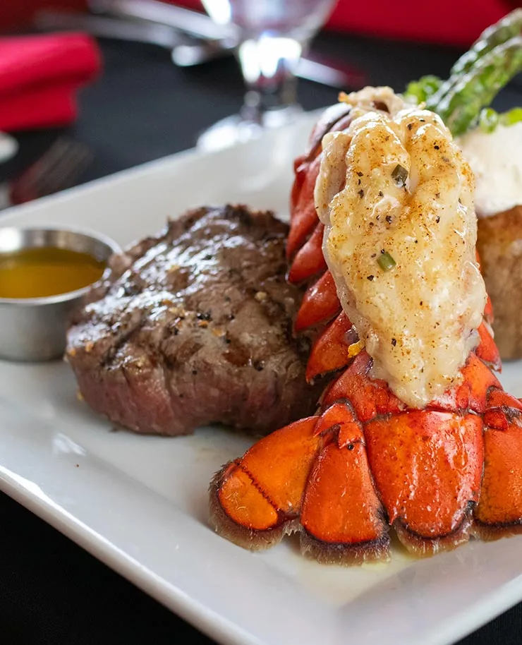 A grilled filet with a broiled lobster tail, asparagus, a baked potato and a cup of drawn butter
