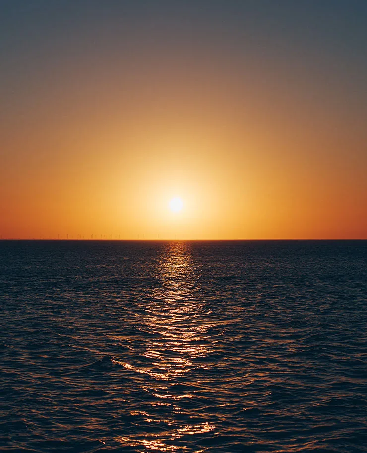 The sun setting over calm water, with a path of light on the waves
