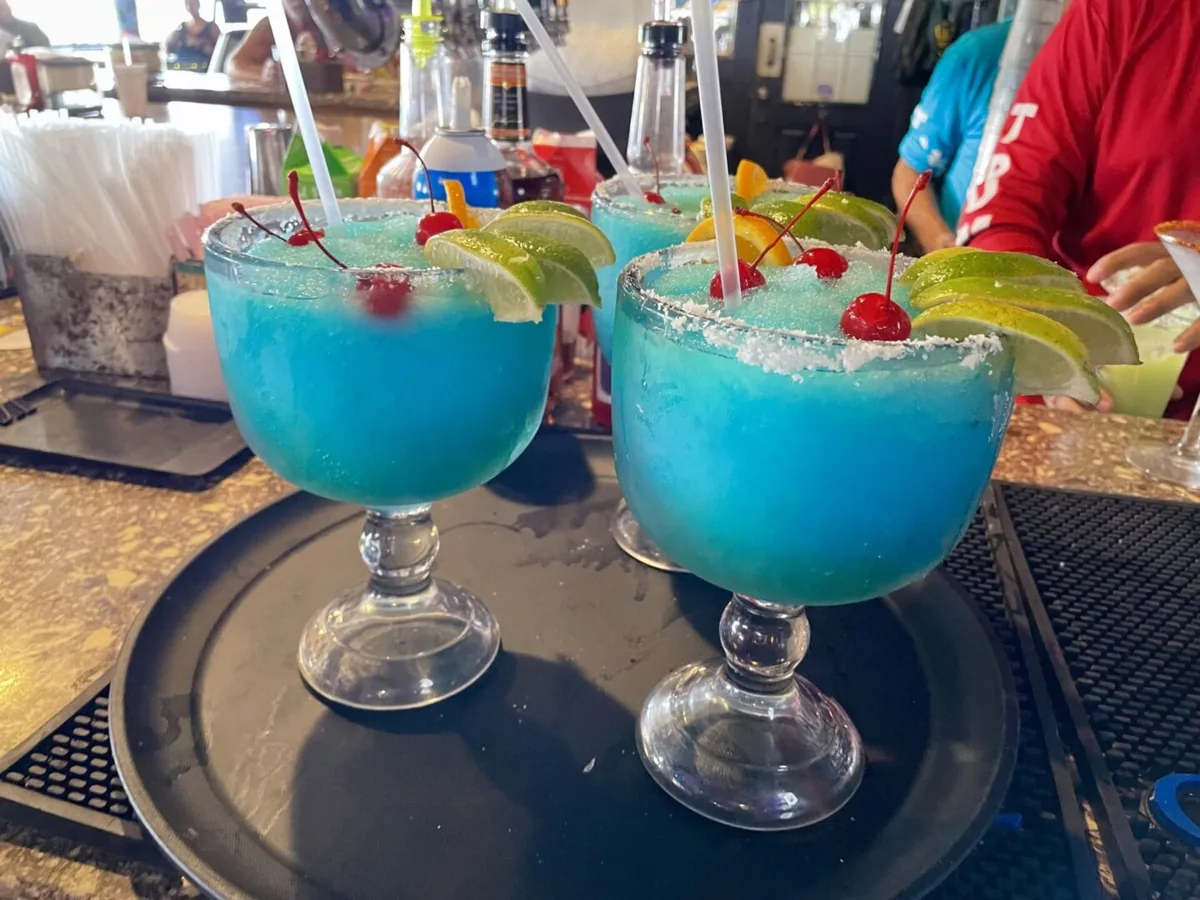 Two blue frozen drinks with sugared rims, cherries, lime and orange slices on a bar tray