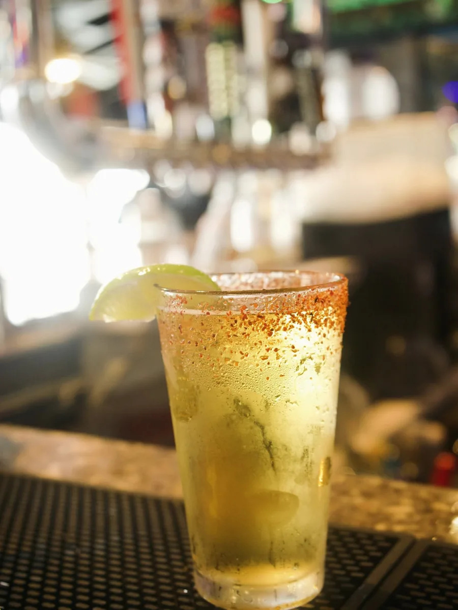 A cold drink in a pint glass with a chili-salt rim and a lime wedge on the bar