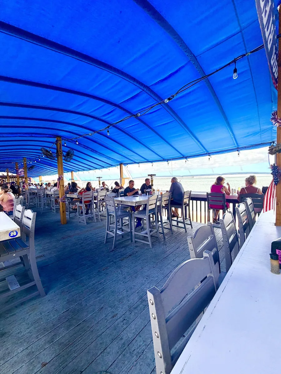 The long covered deck under a blue canopy, with tables along the rail over the bay