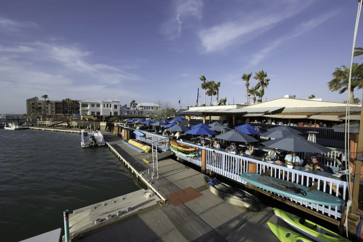 The waterfront deck with blue umbrellas beside the docks, with kayaks and paddleboards along the rail