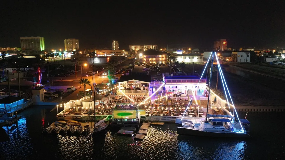 An aerial night view of the lit-up decks, piers and a catamaran strung with lights