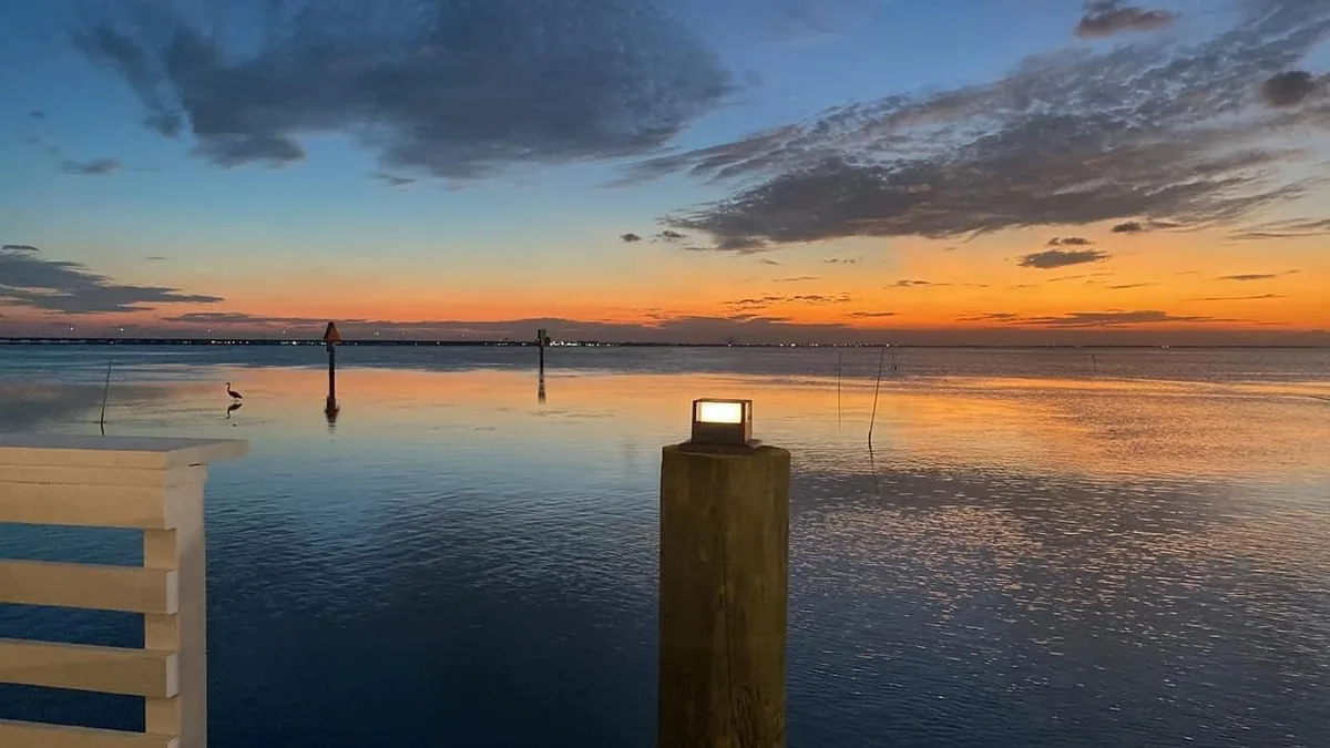 Calm water and a lit piling at the end of the deck at sunset