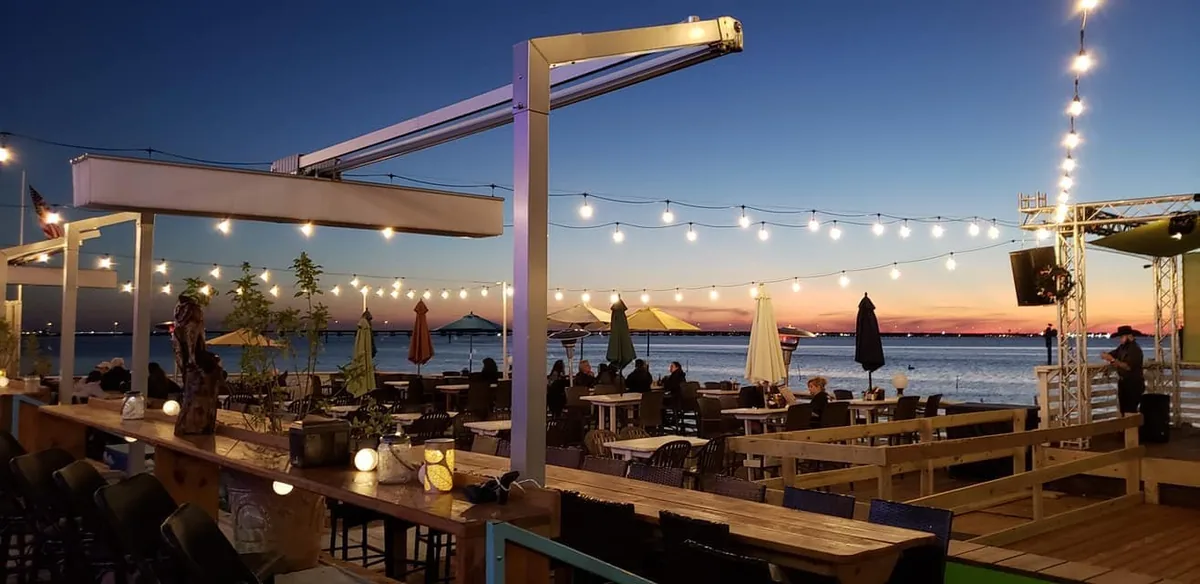 The waterfront deck with long tables under string lights at sunset
