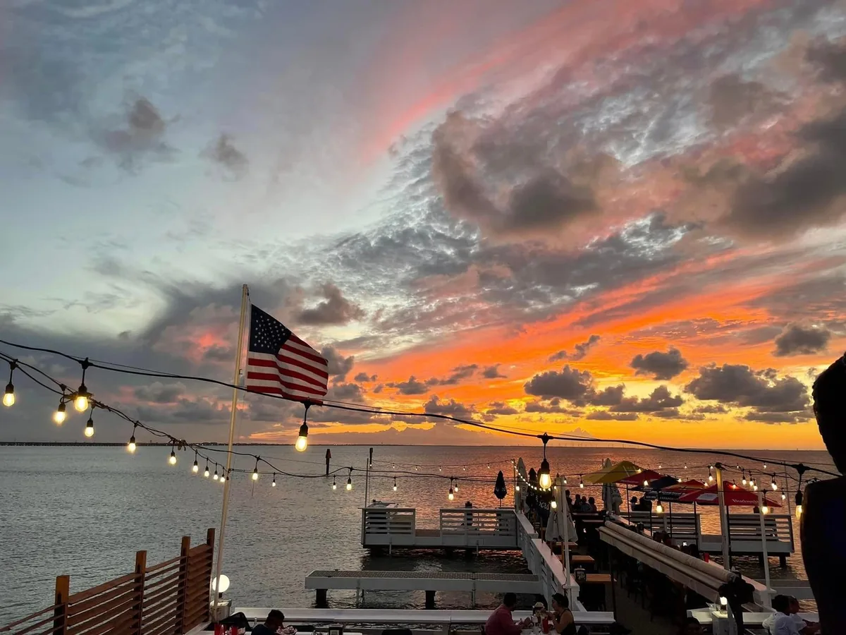 An American flag and string lights over the piers as the sun sets over the bay
