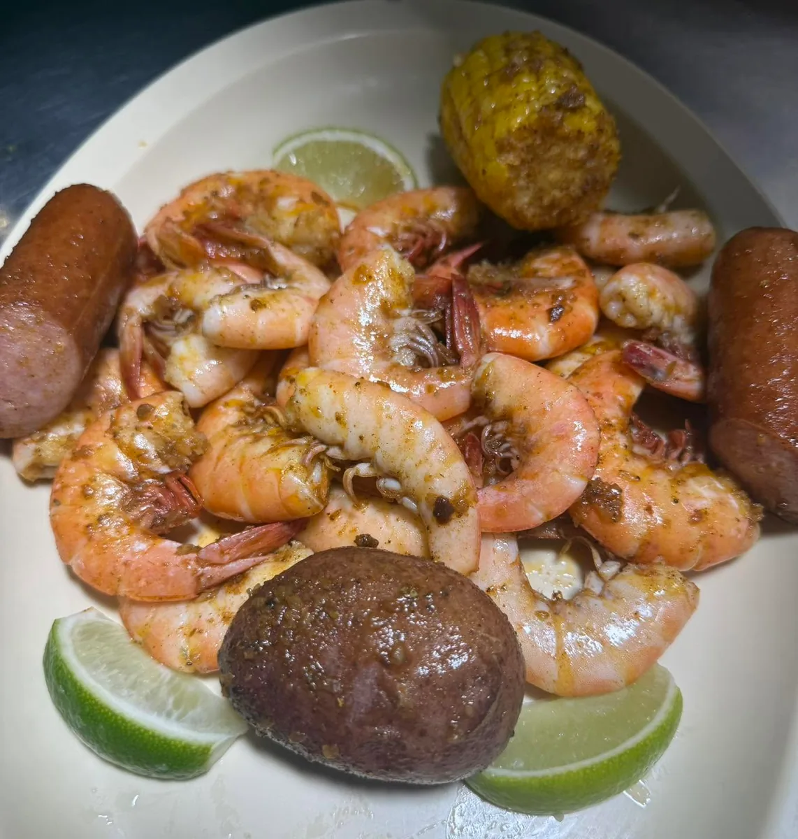 A plate of Cajun-seasoned boiled shrimp with sausage, corn on the cob, a potato and lime