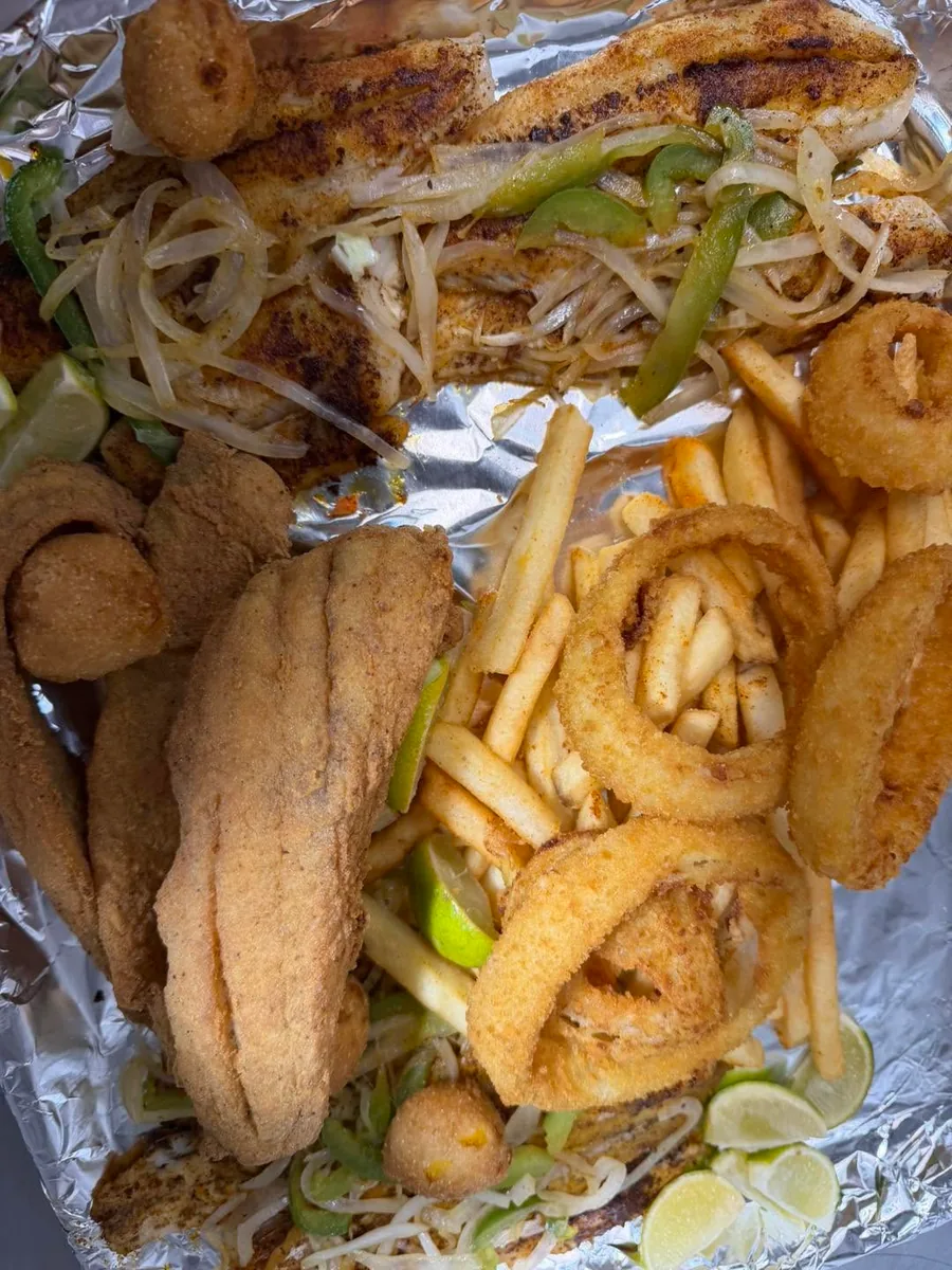 Fried and grilled fish fillets with onion rings, fries, hush puppies and grilled onions in a foil tray