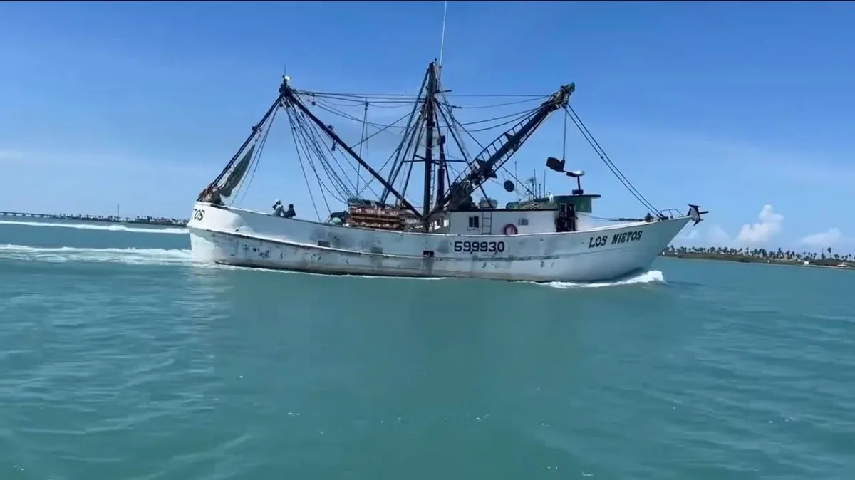 A shrimp boat with its rigging up, cruising through the channel