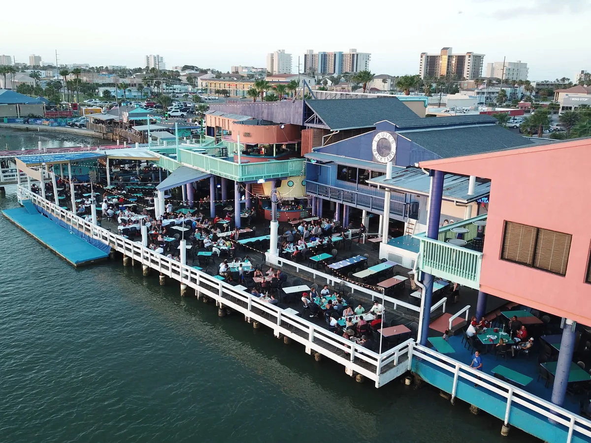 An aerial view of Louie's Backyard on the Laguna Madre: the pink and blue building, the long bay-front deck and the water