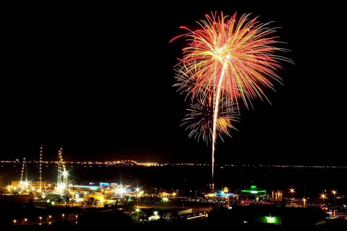 Fireworks bursting over the bay at night, with the lights of the shore below