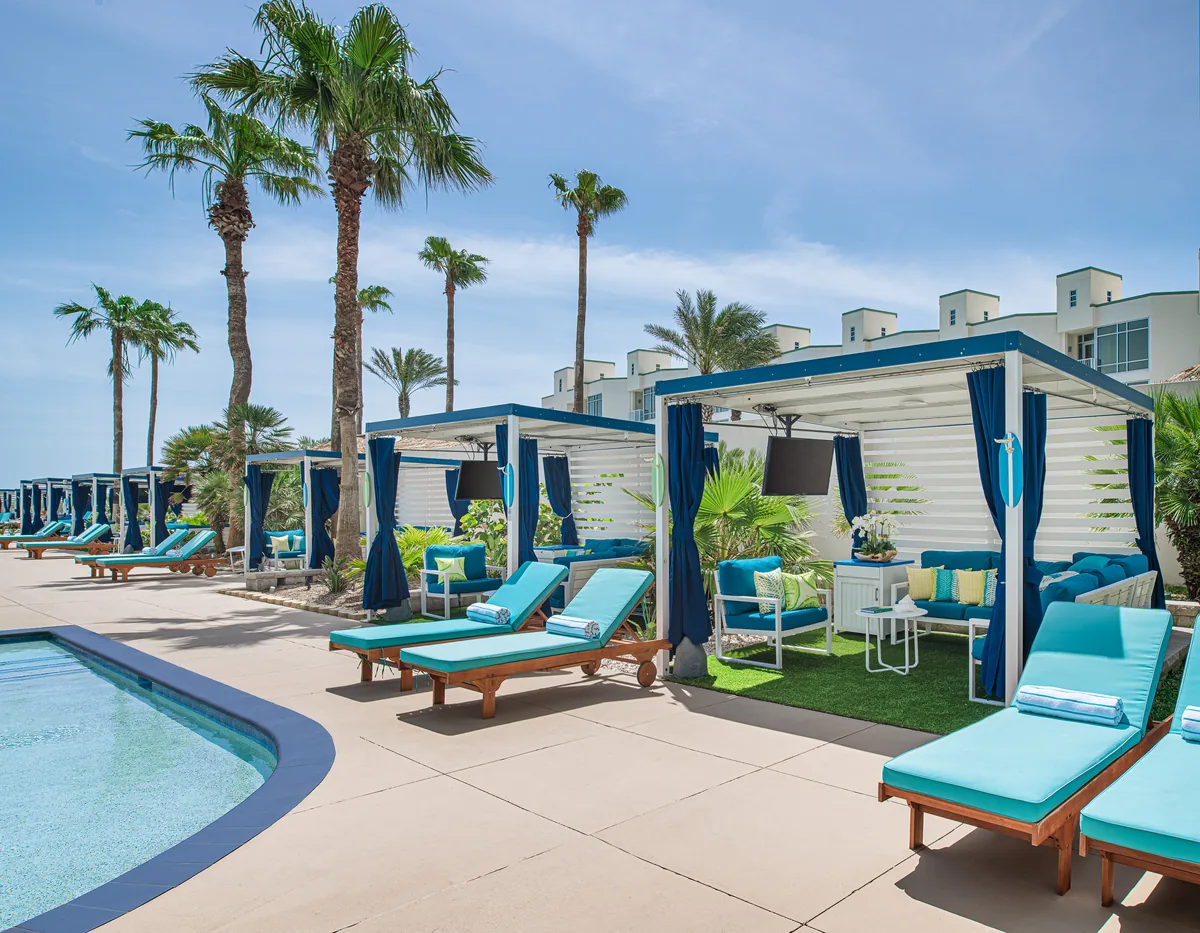 Poolside cabanas with navy curtains and turquoise loungers under palm trees
