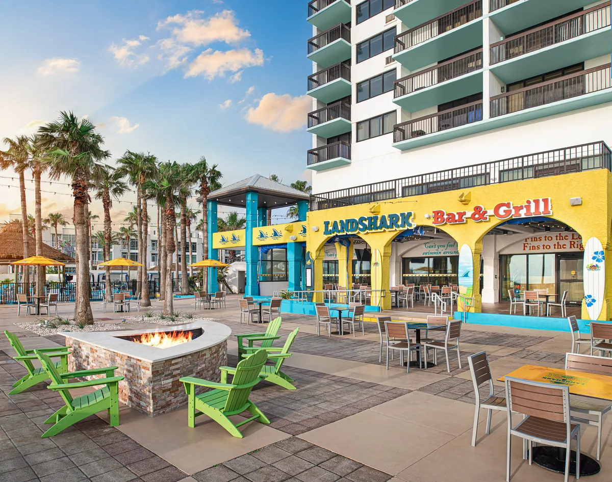 The courtyard with a fire pit and green Adirondack chairs in front of the yellow LandShark Bar & Grill
