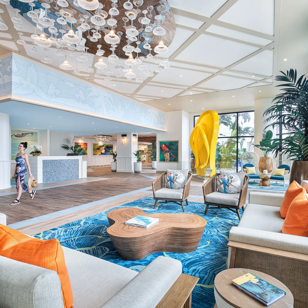 The resort lobby with a blue rug, white sofas, orange cushions and a giant yellow flip-flop sculpture