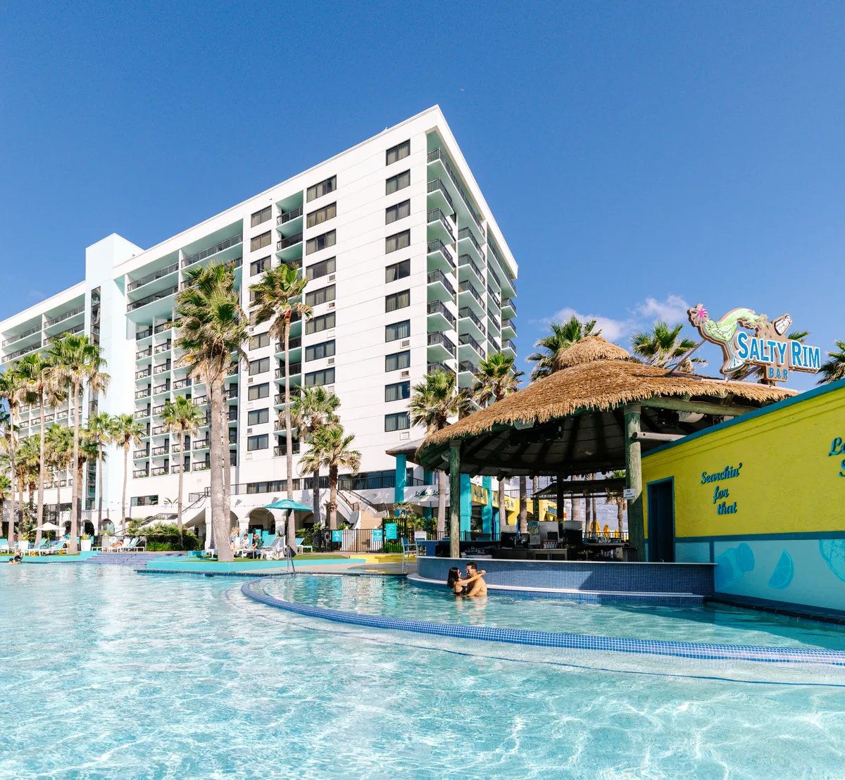The resort pool with the thatched Salty Rim swim-up bar, palms and the hotel tower behind