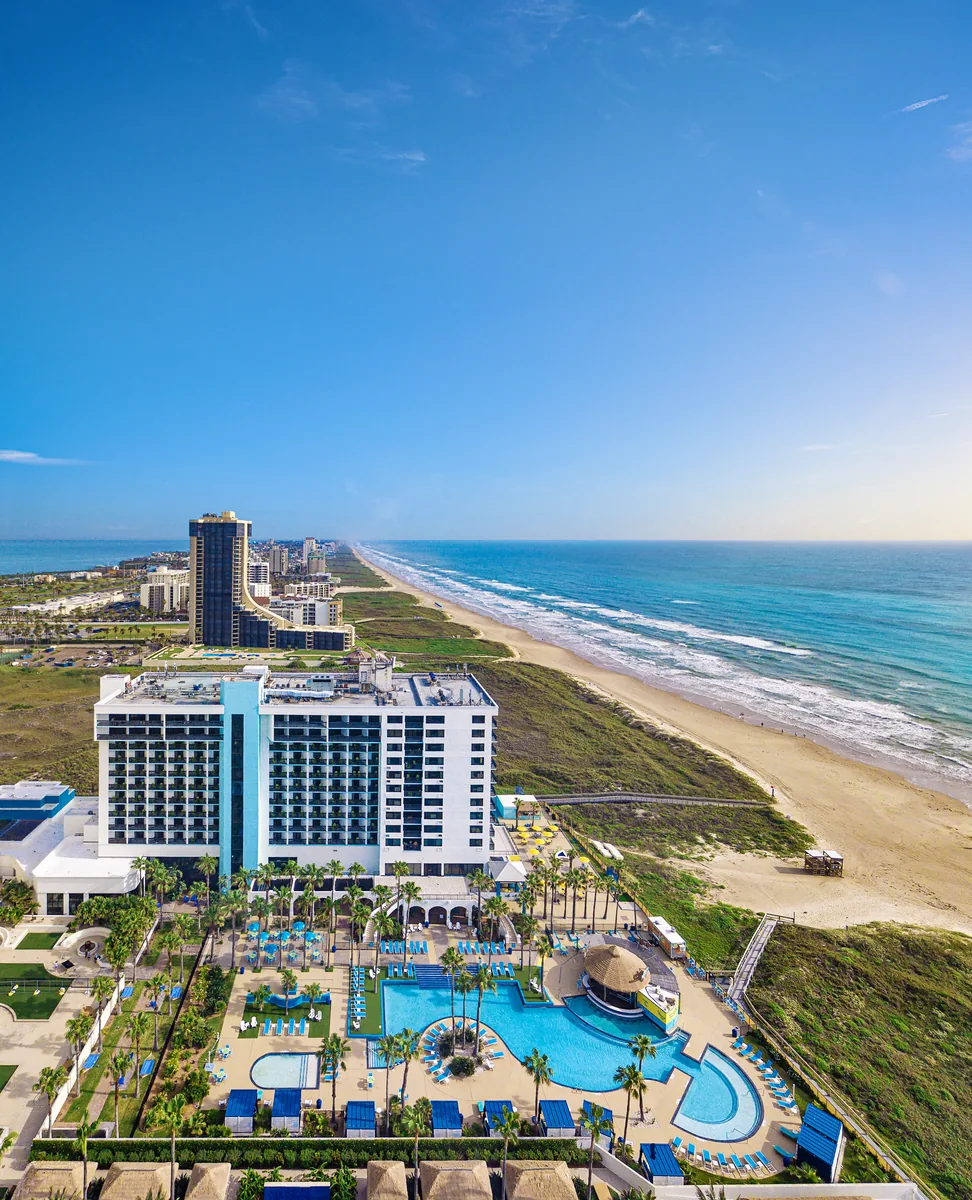 An aerial view of the resort tower, its pool and the beach stretching north along the Gulf
