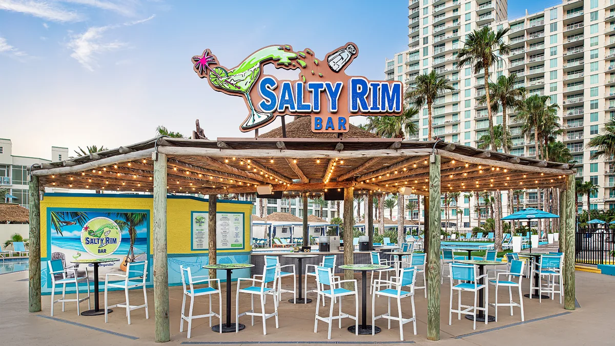 The Salty Rim Bar under a wooden pergola with string lights and blue bar stools by the pool