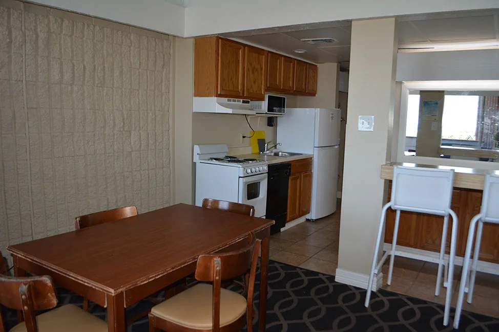 A room kitchen with a stove, a full-size refrigerator, cabinets, a dining table and a breakfast bar