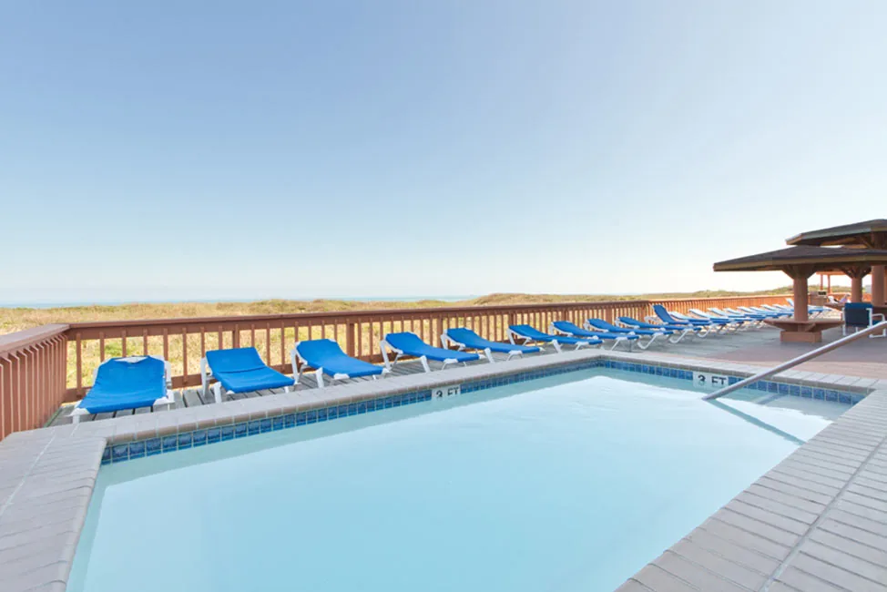 The pool with blue loungers along the deck rail above the dunes